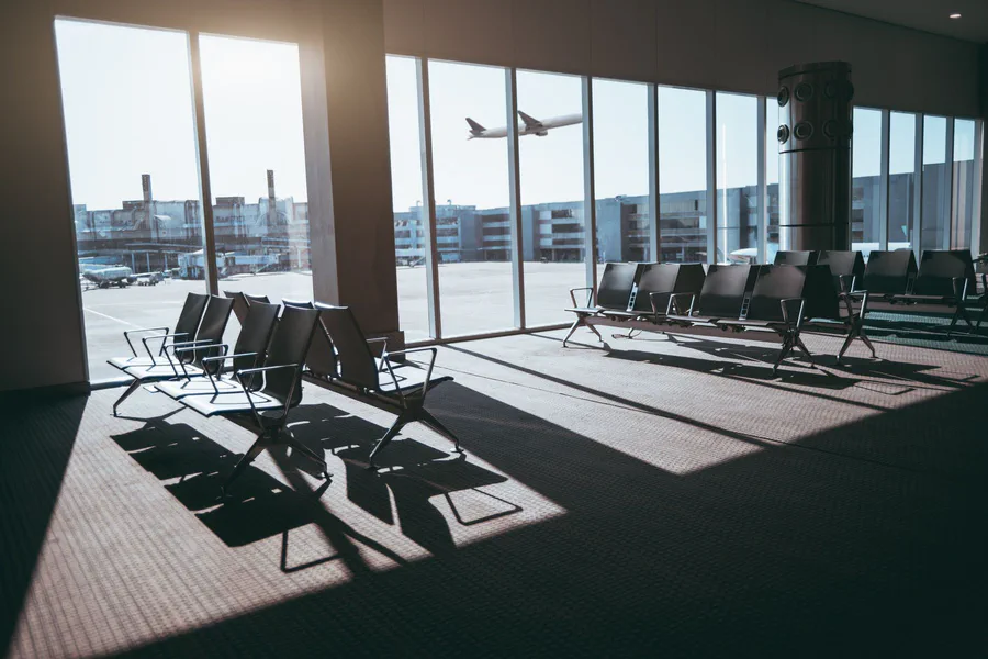Sedili vuoti in una sala d'imbarco con il sole basso e un aereo che sale oltre la vetrata