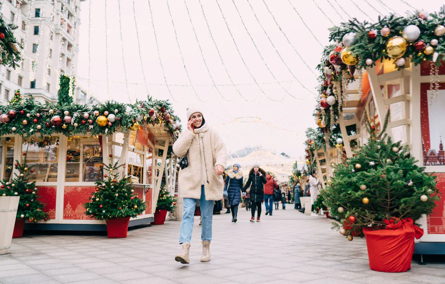Un pasillo de mercadillo navideño a plena luz del día, con algunas personas caminando entre puestos decorados