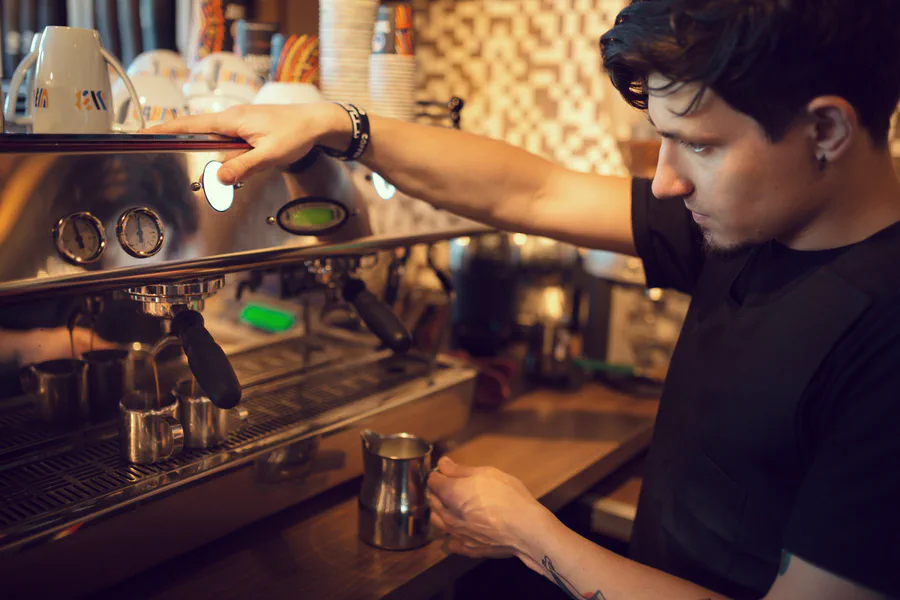 Un barista manejando una máquina de café profesional detrás de una barra de acero inoxidable