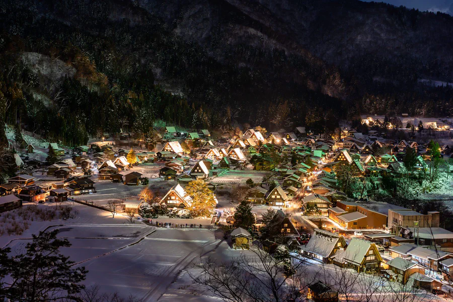 Thatched farmhouses in Shirakawa-go lit up at night under snow