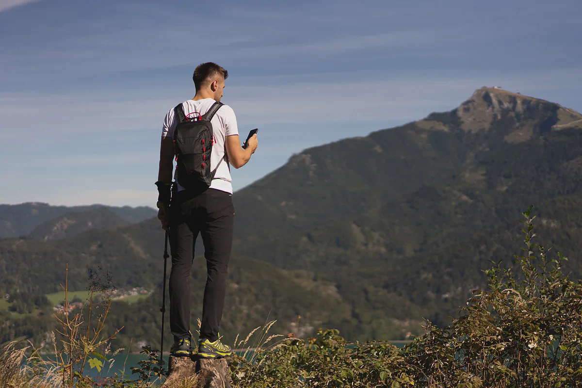 Un escursionista guarda il telefono in cima a una collina, con le montagne alle spalle