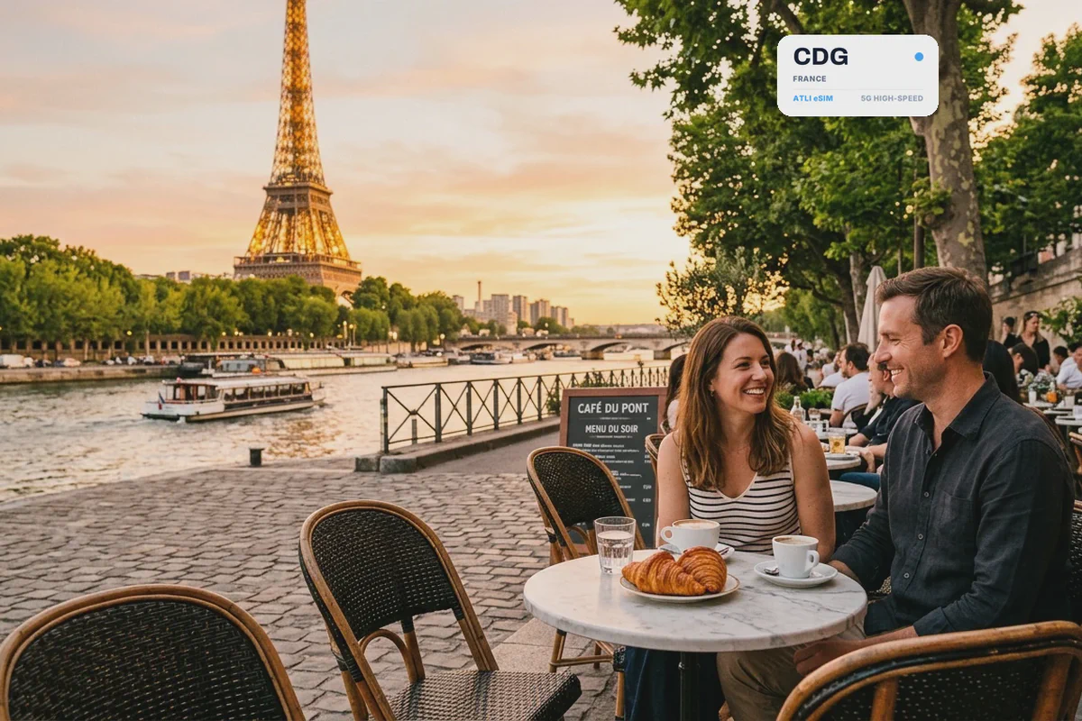 Una coppia al tavolino di un caffè parigino, con la Torre Eiffel dietro, con una scheda eSIM Atli che mostra il codice aeroportuale CDG