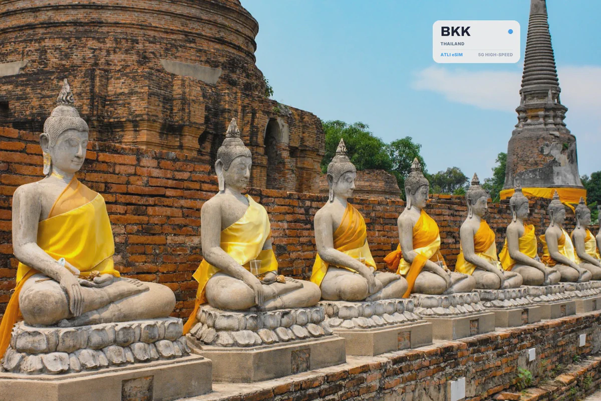 Una fila di statue di Buddha in vesti color zafferano accanto agli stupa di mattoni di Ayutthaya, con una scheda eSIM Atli che mostra il codice aeroportuale BKK