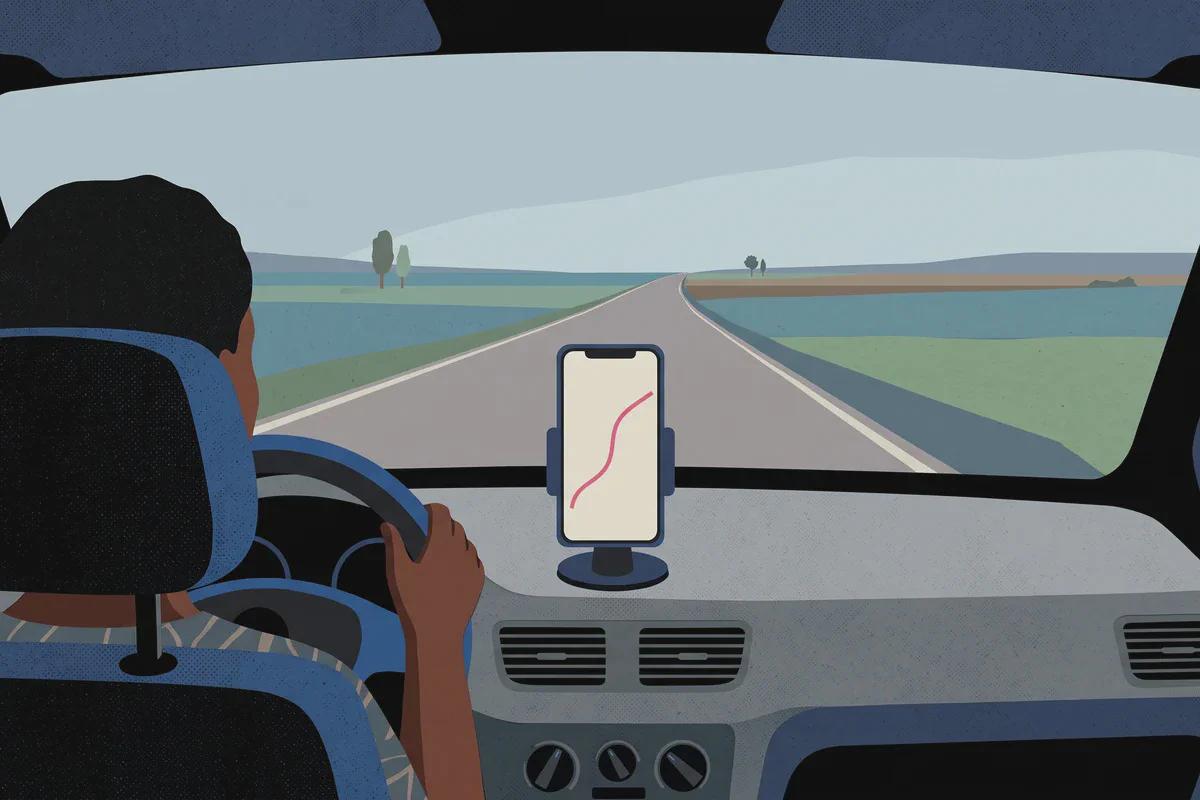 Ein Handy am Armaturenbrett zeigt eine Navigationsroute, davor die Straße durch die Windschutzscheibe