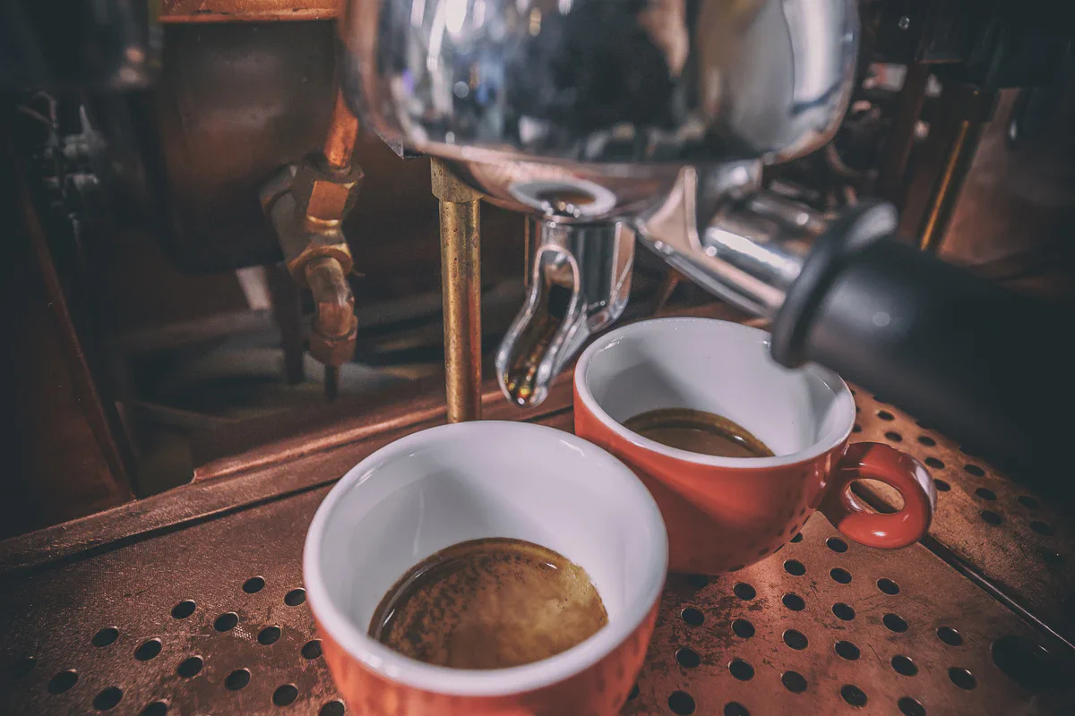 Dos tazas de cerámica con café expreso recién servido y crema dorada bajo una cafetera profesional