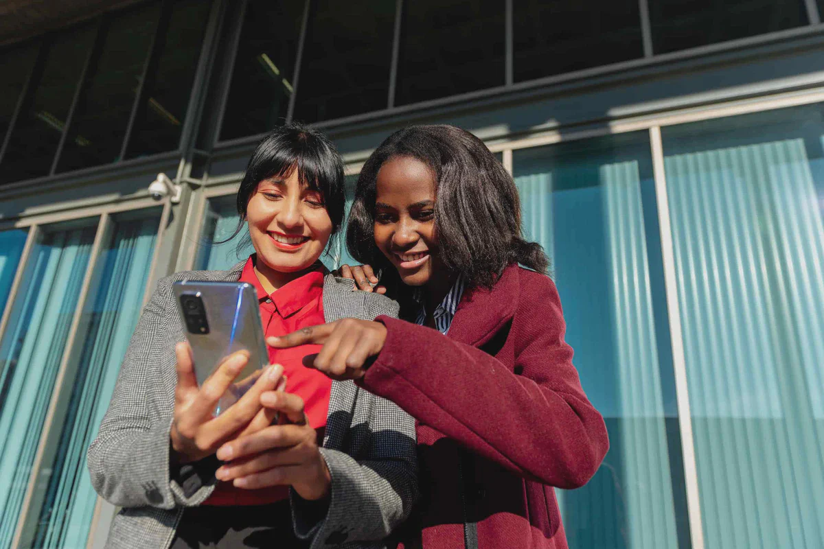 Due donne all’aperto guardano insieme lo schermo di un telefono