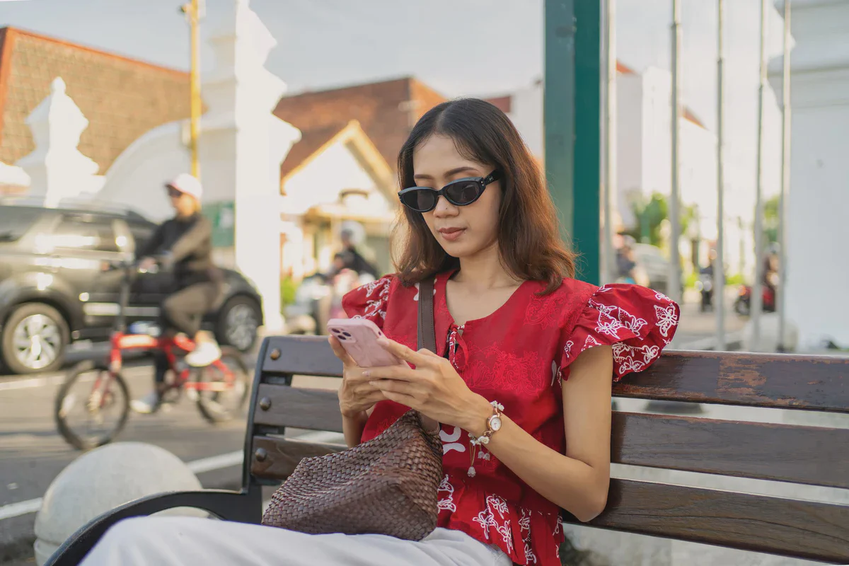 Una donna seduta su una panchina usa il suo iPhone, il traffico passa alle sue spalle