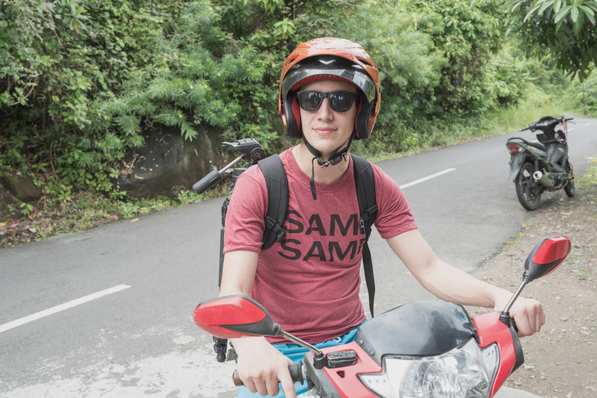 Un motociclista con casco allacciato seduto su uno scooter su una strada nella giungla