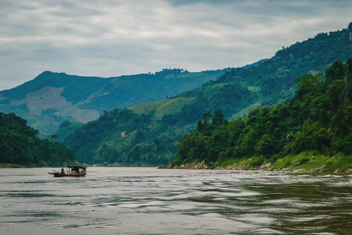 A small boat on the wide Mekong below forested ridges