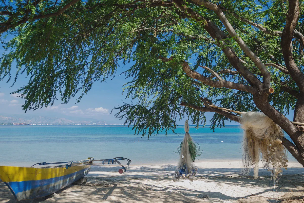 Una barca con bilanciere e reti stese ad asciugare sulla spiaggia di Areia Branca, a Dili