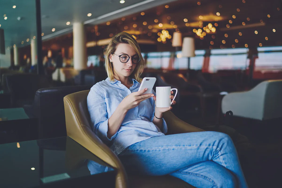 Una donna con il telefono e un caffè in poltrona in una lounge